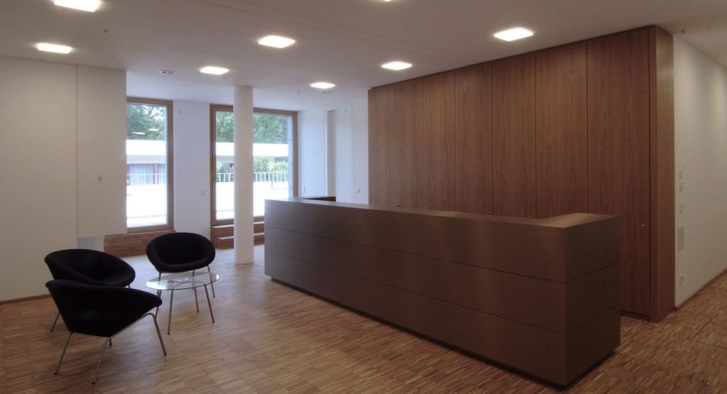 Empfangstheke aus dunklem Holz in einem hellen Raum mit Sesseln